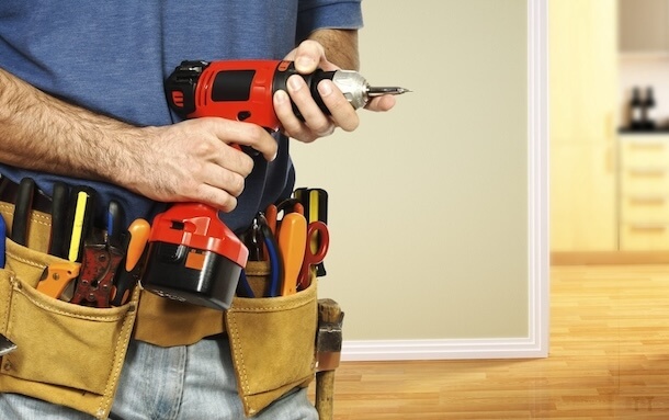 Handyman with a tools belt holding a red drill in his hands